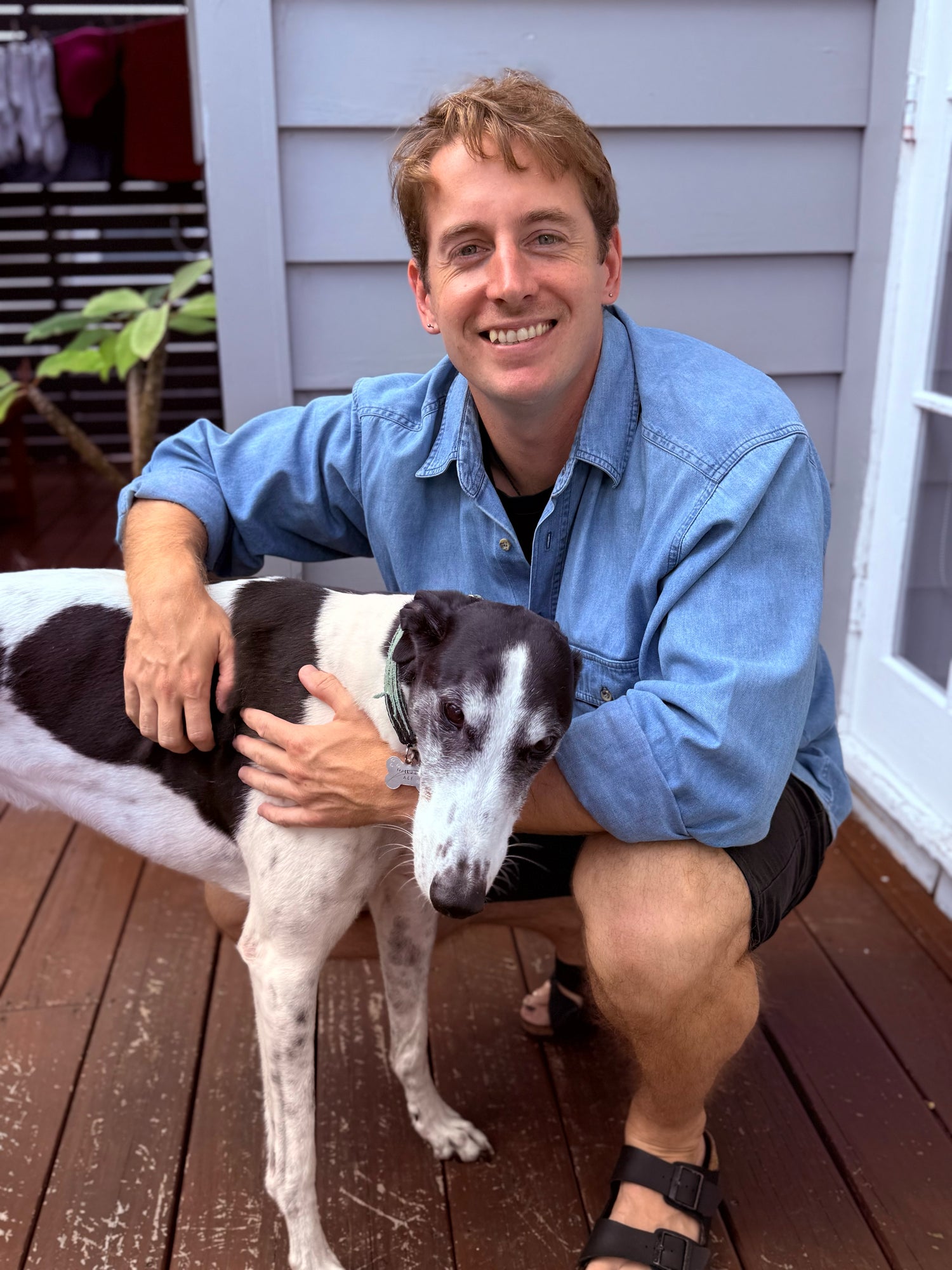 Man sitting on a wooden deck with a black and white dog. Best supplements for dogs in the USA